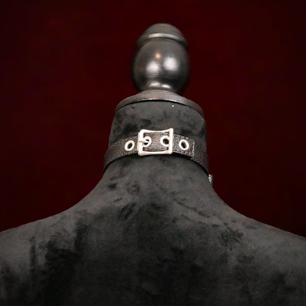 Black mannequin with a silver buckle against a dark red background