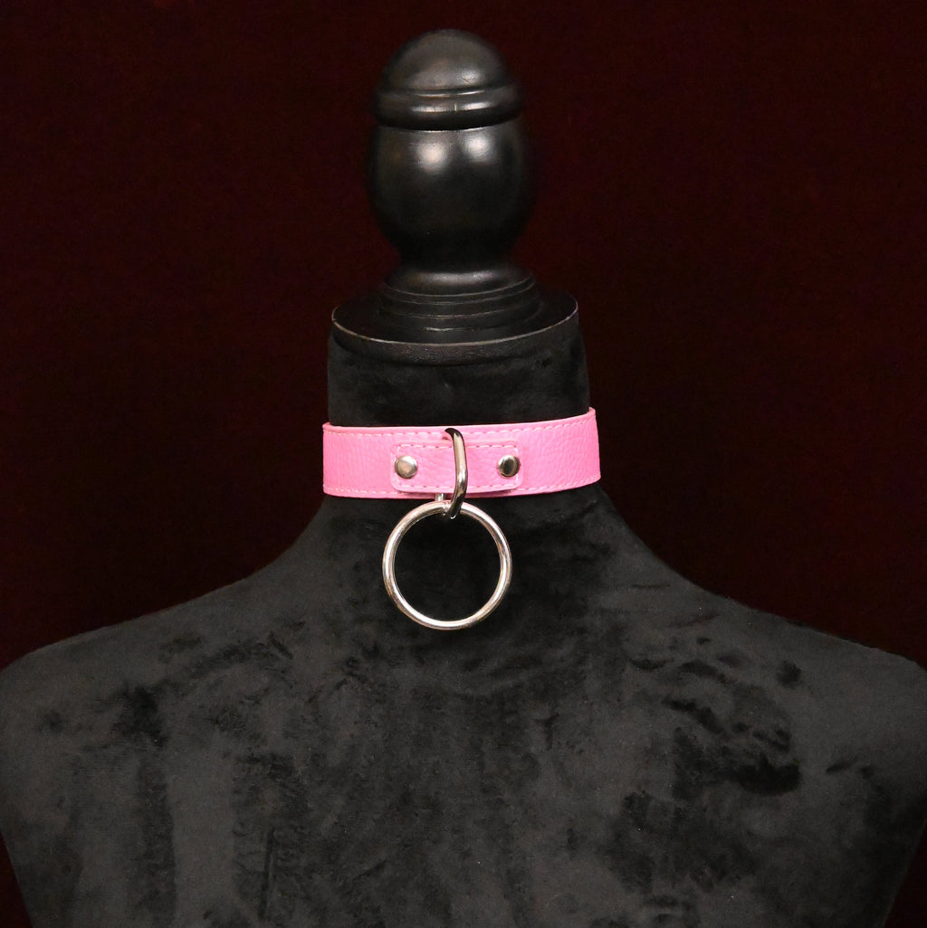 Pink leather collar with silver O ring on a black mannequin against a dark red background