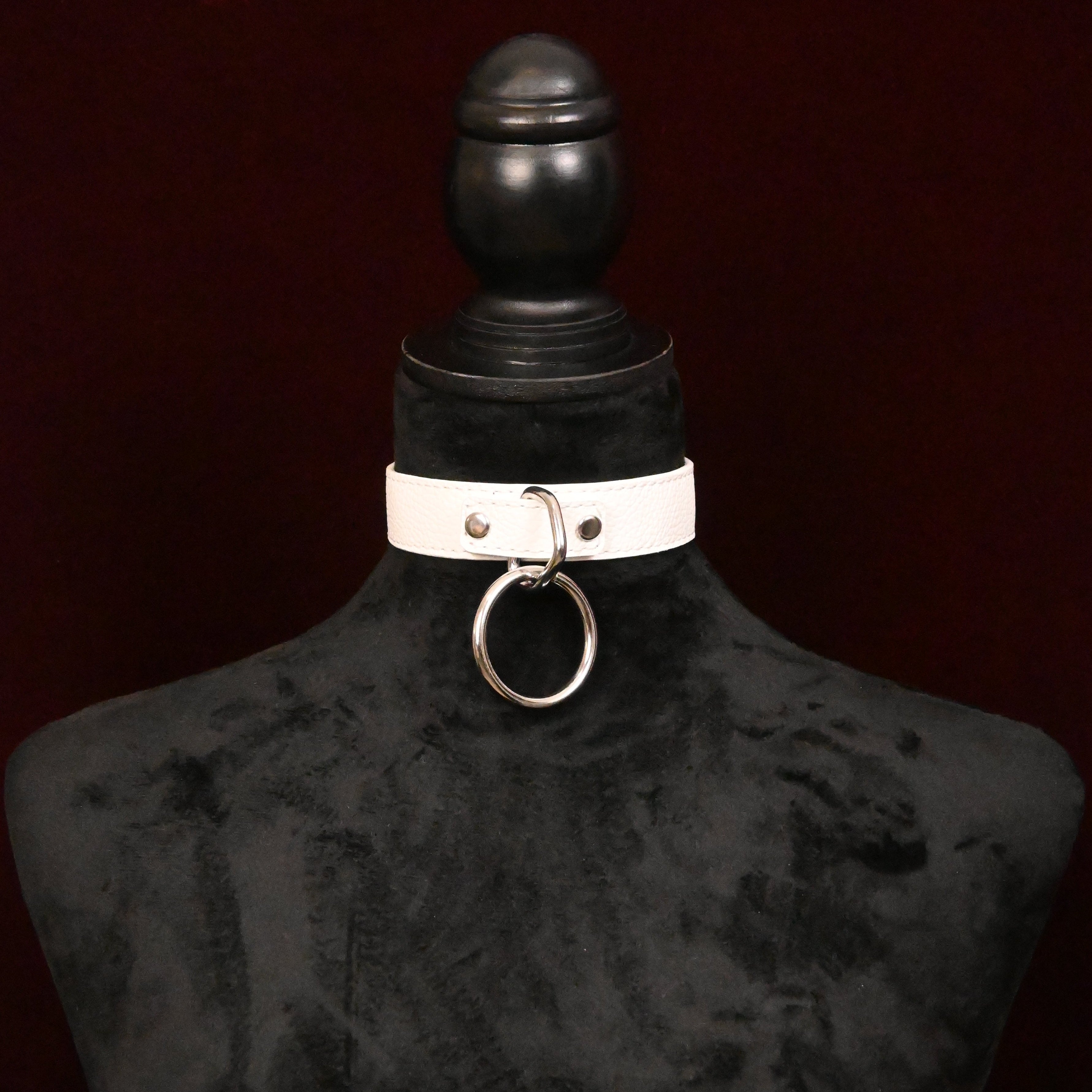 White leather collar with silver O ring on a black mannequin against a dark red background