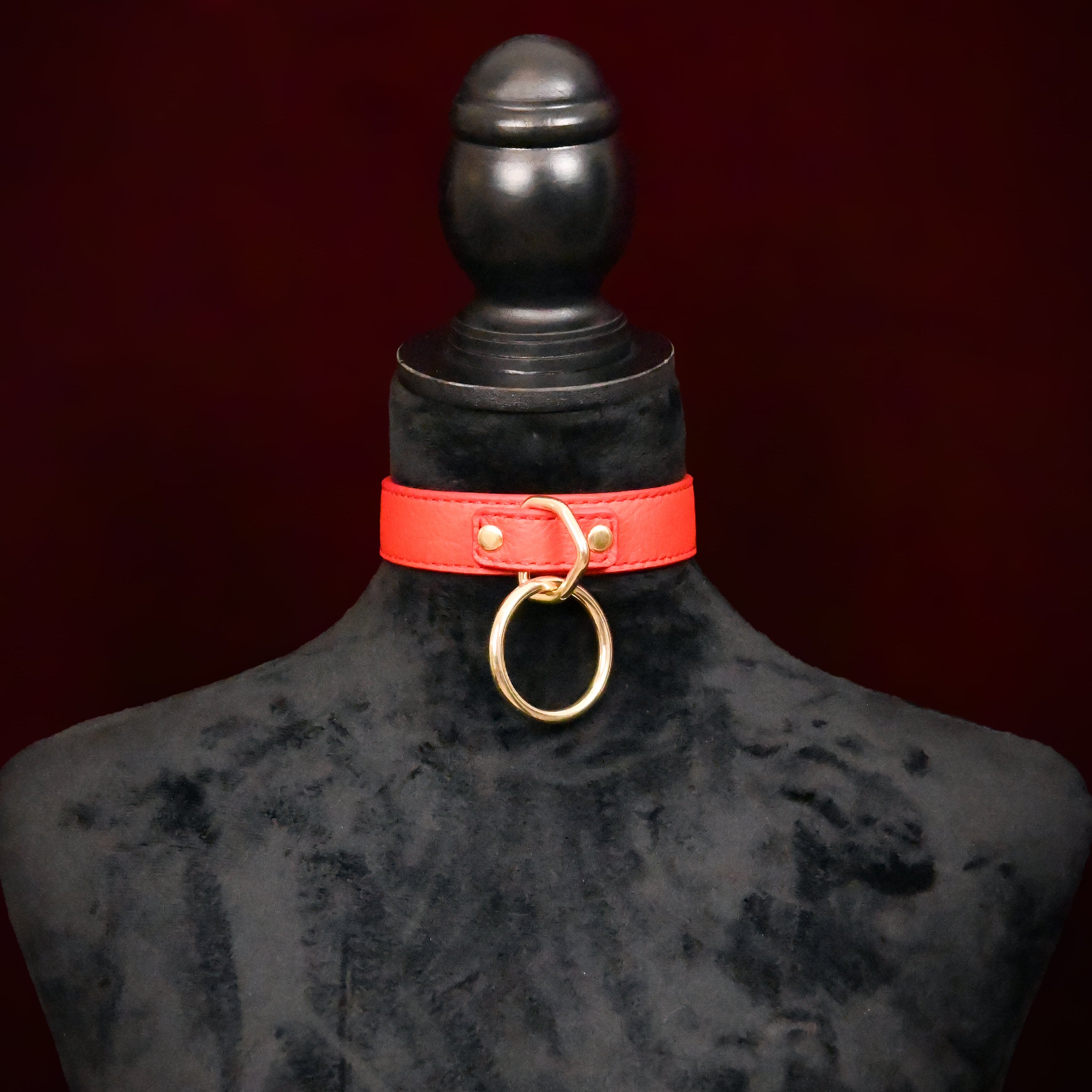 Red leather choker with gold ring on a black mannequin against a dark background