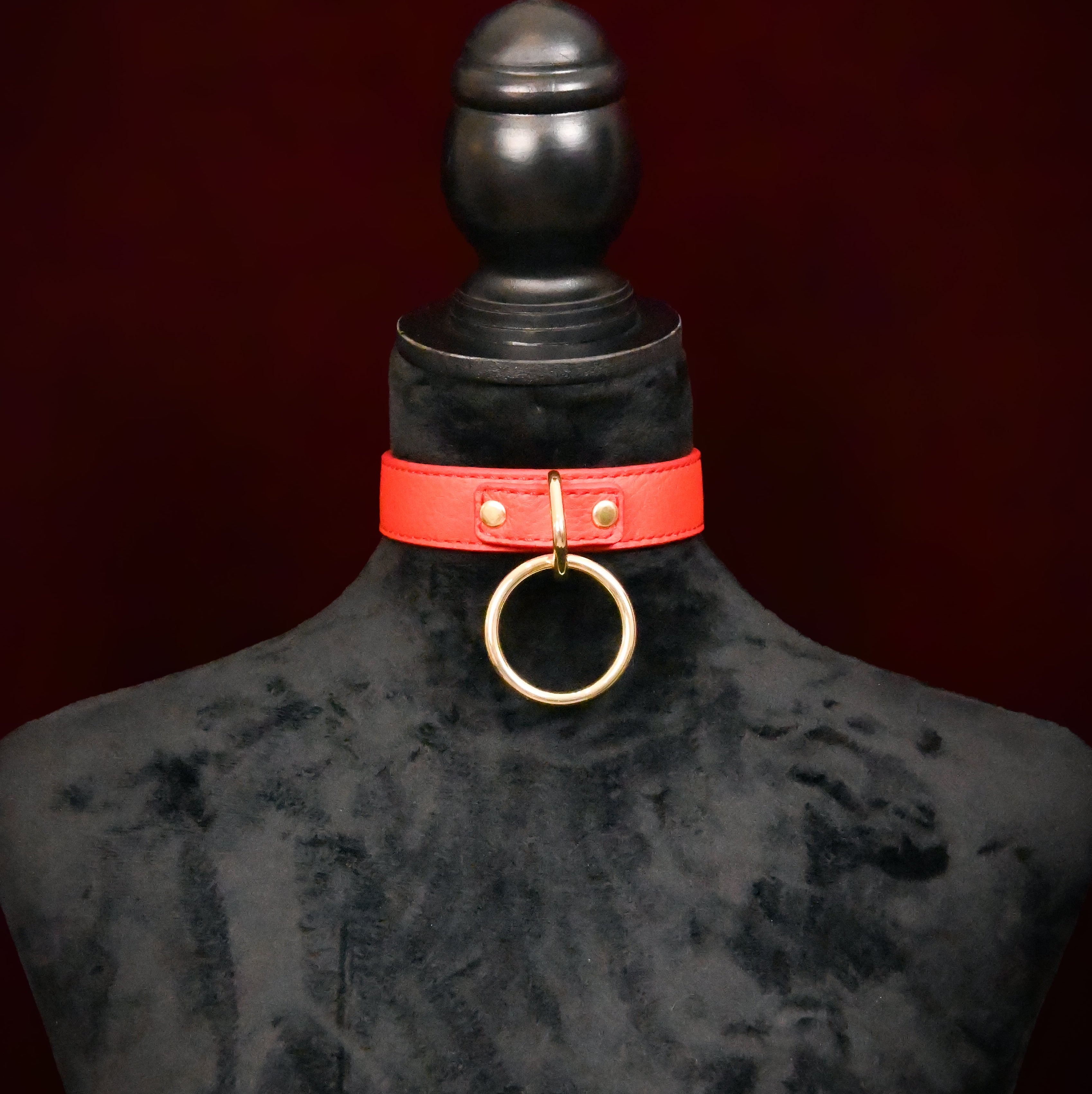 Red leather choker with gold ring on a black mannequin against a dark background