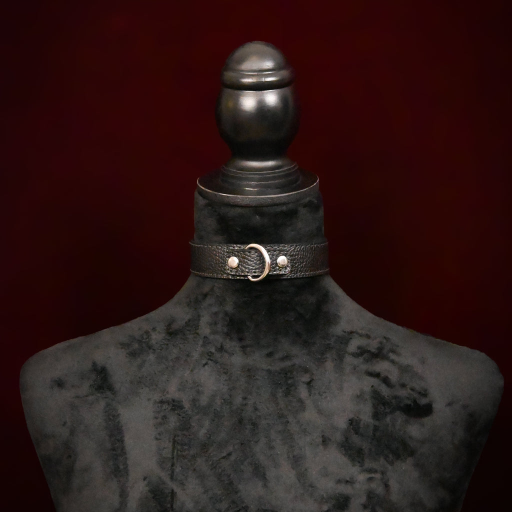 Black leather choker with silver rings on a mannequin against a dark background