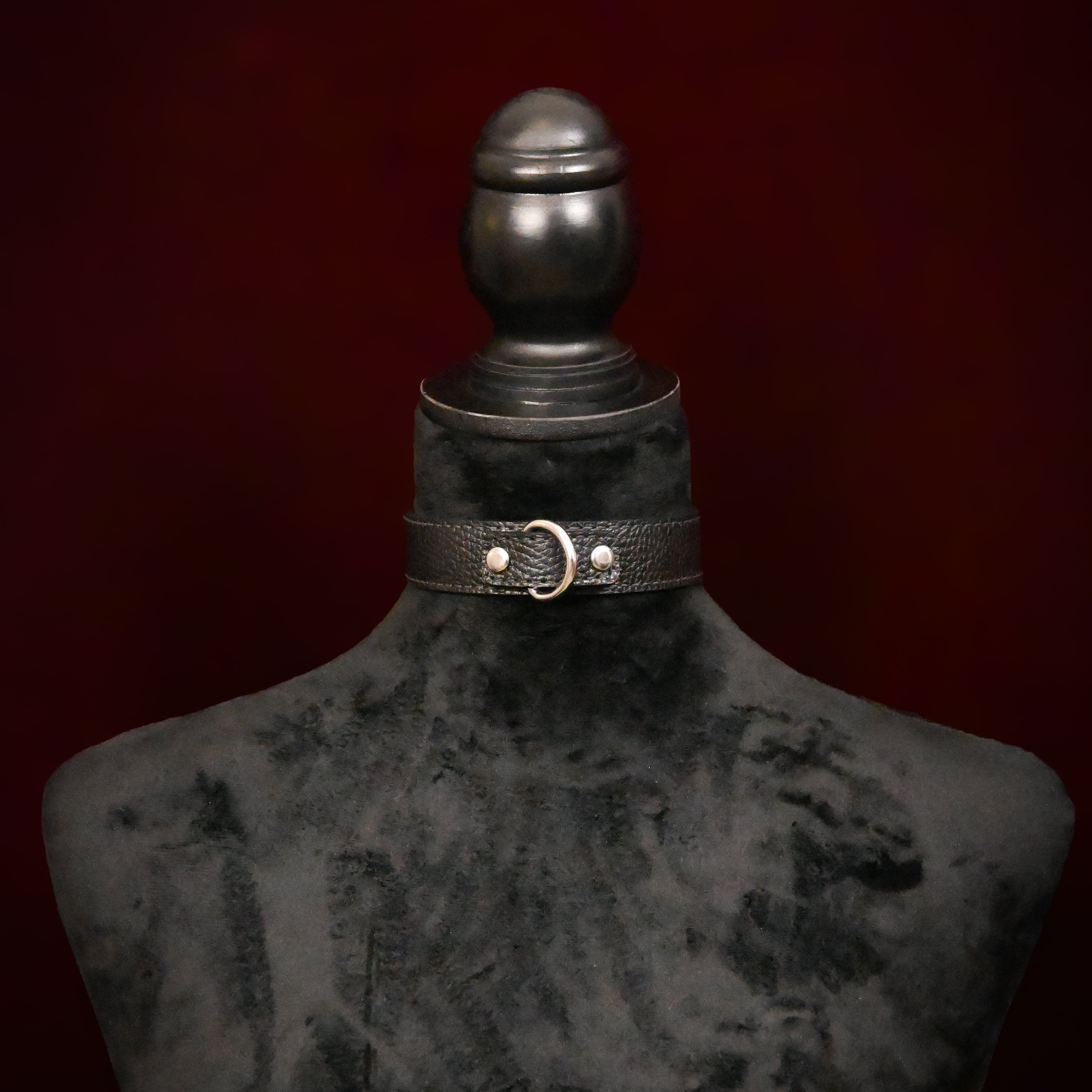 Black leather choker with silver rings on a mannequin against a dark background