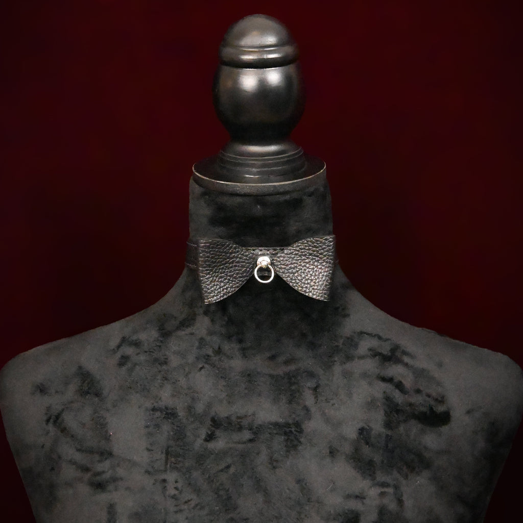 Black collar with bow and silver ring on a black mannequin on dark background