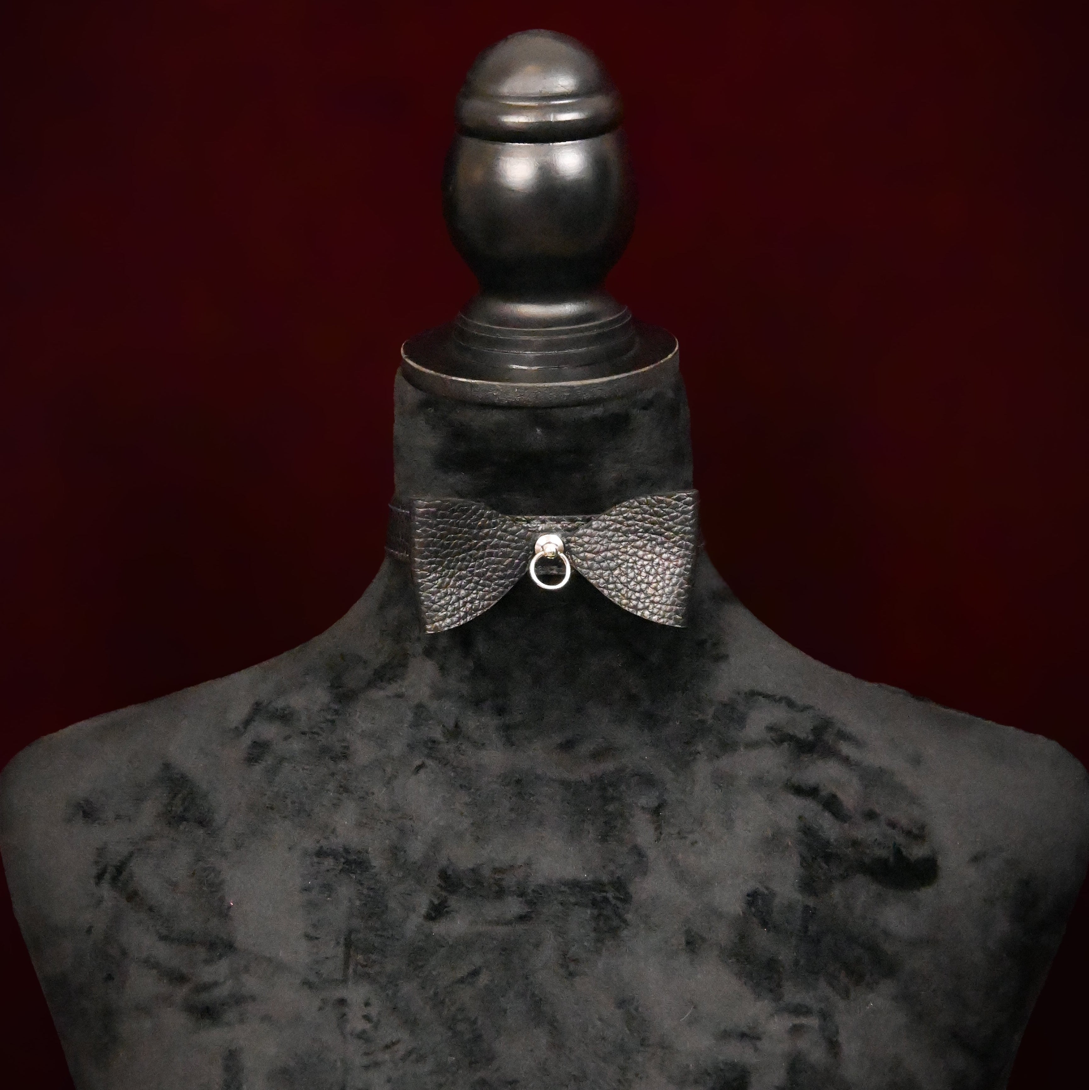 Black collar with bow and silver ring on a black mannequin on dark background