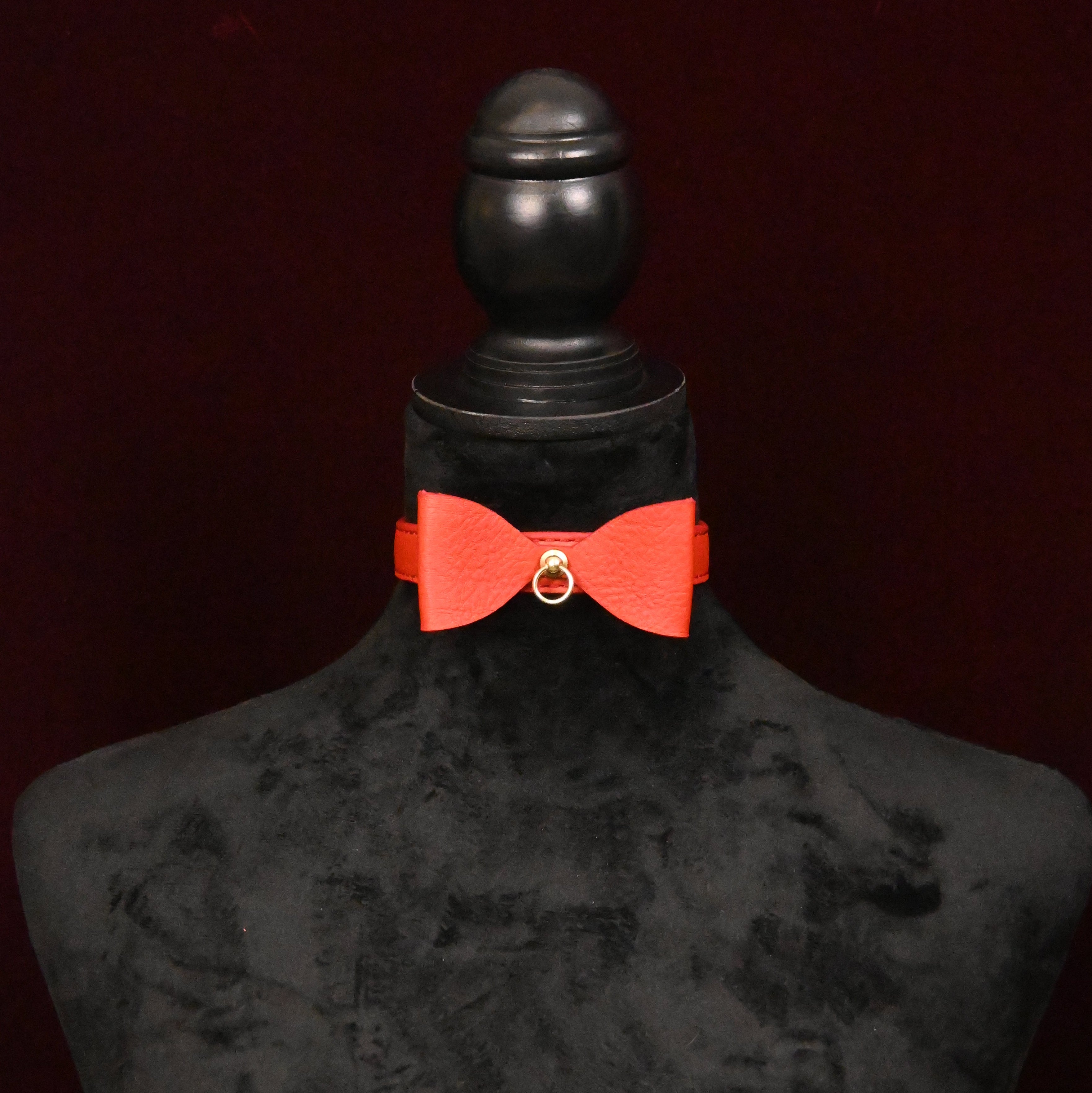 Red bow collar on a black mannequin with a dark background