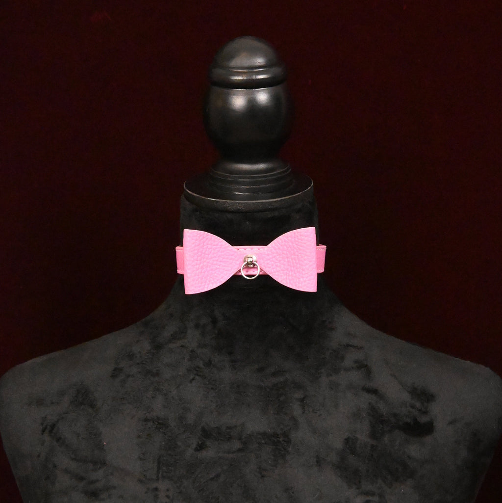 Pink collar with bow and silver ring on a black mannequin on dark background
