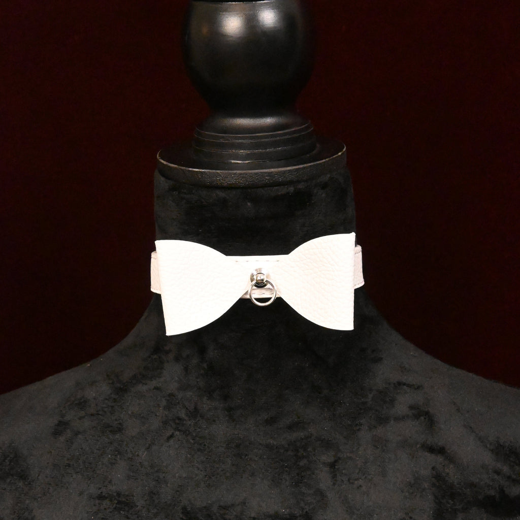White collar with bow and silver ring on a black mannequin on dark background