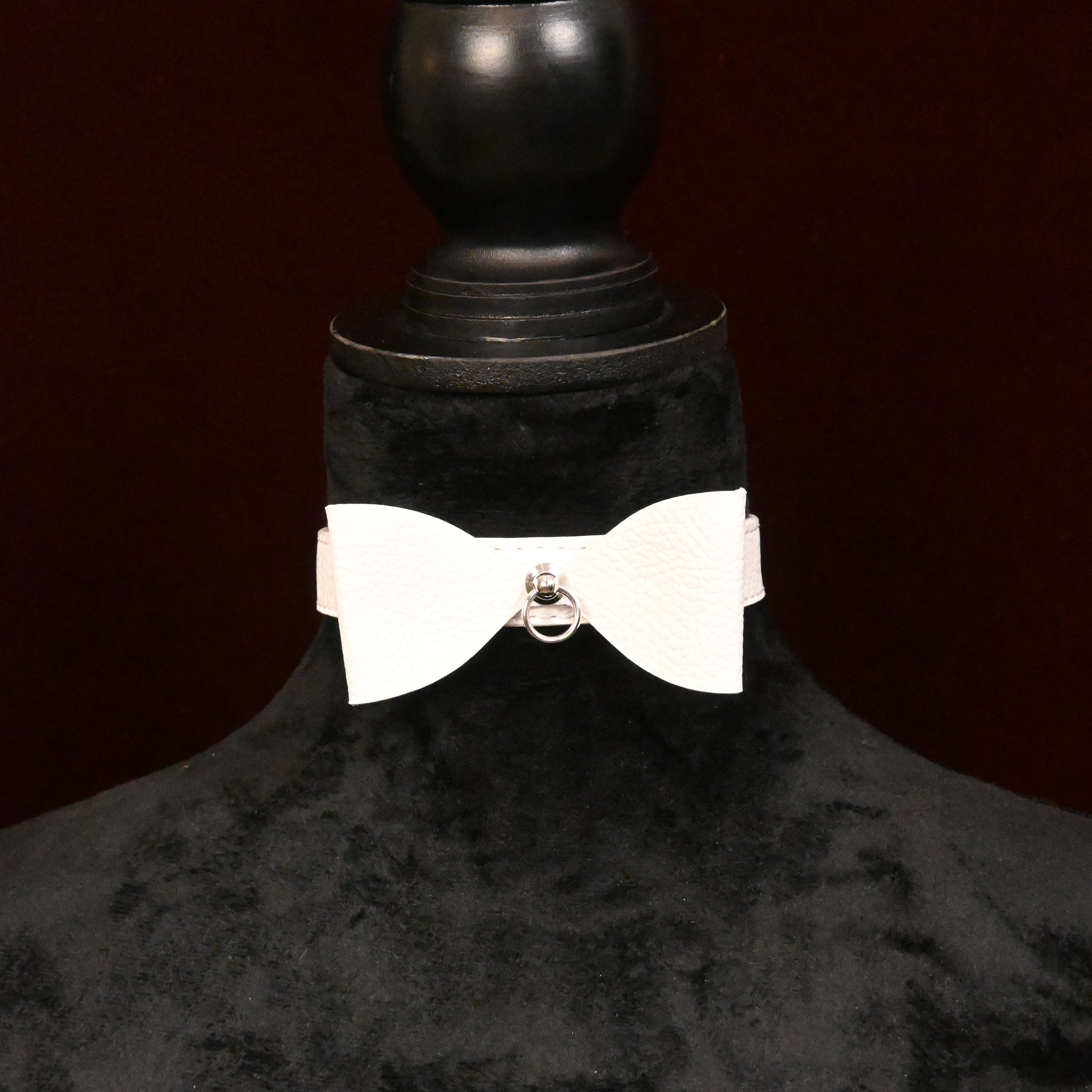 White collar with bow and silver ring on a black mannequin on dark background