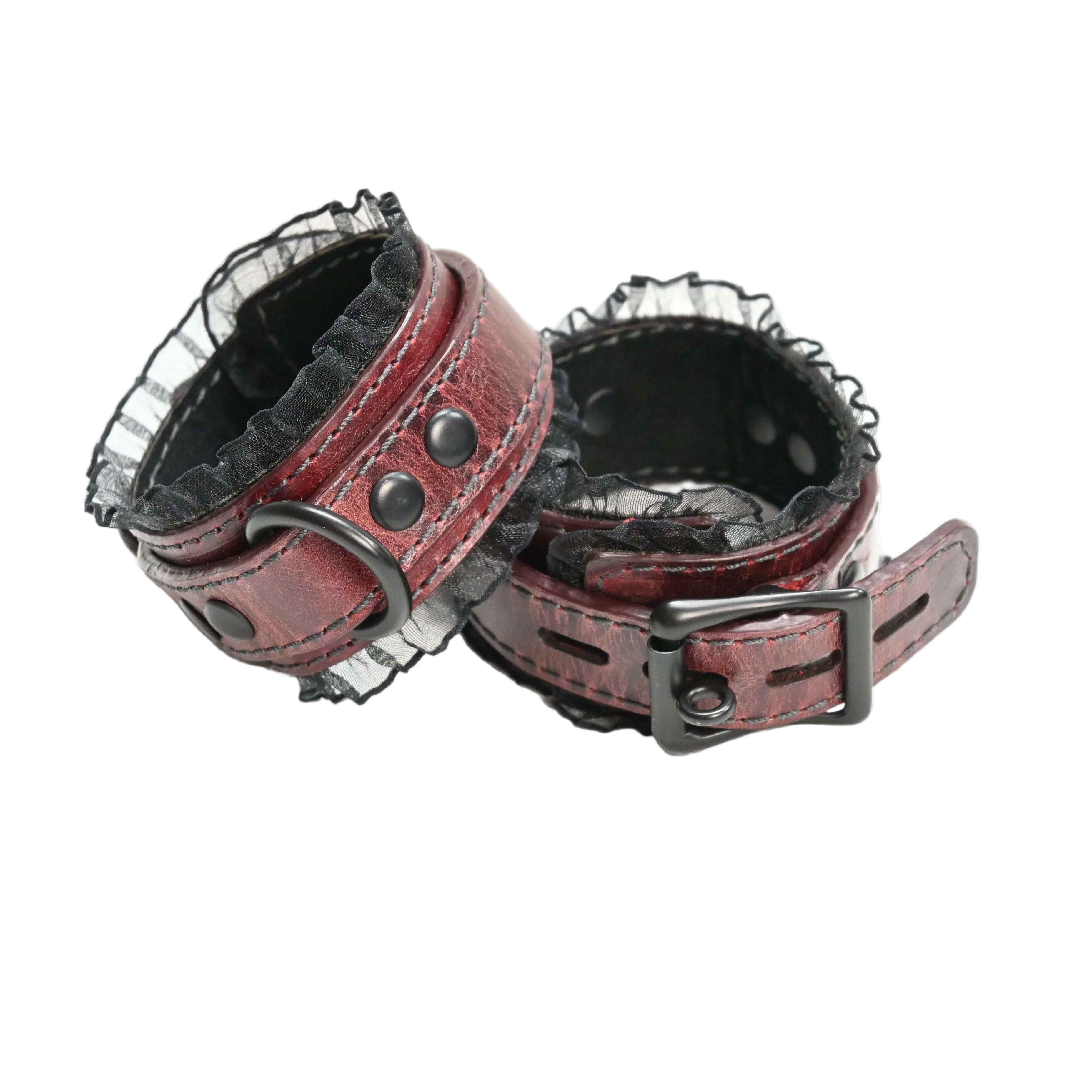 A pair of red leather wrist cuffs with black lace trim, black suede lining, and black metal rings and rivets, photographed on a plain white background.