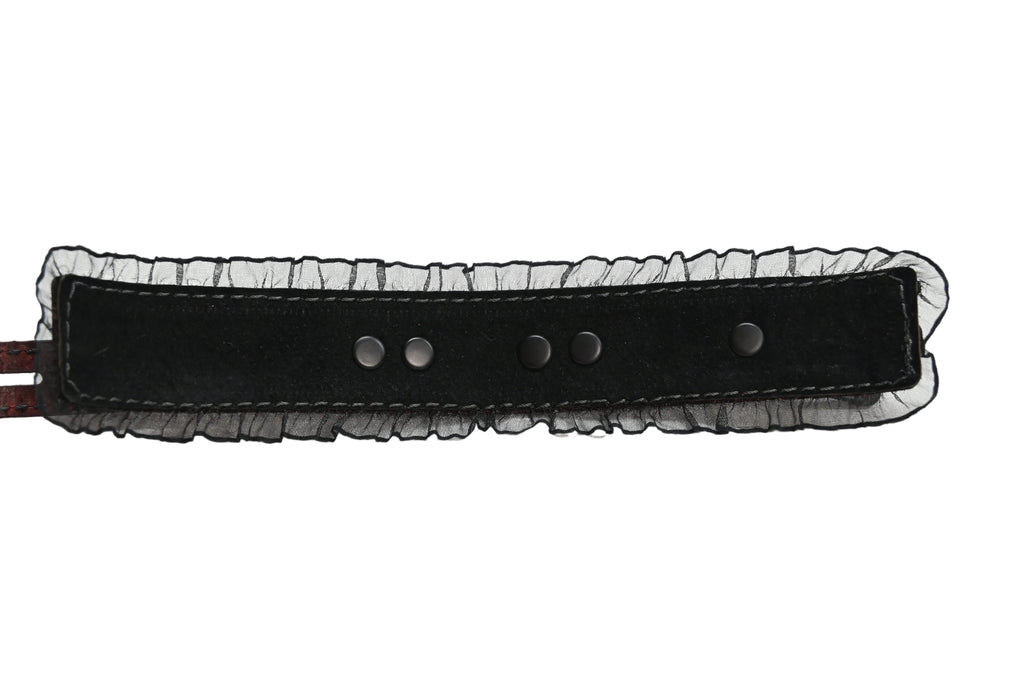 Interior photo of one of the cuffs showing a black suede lining and black ruffles along the edges, and black rivets. Photographed on a white background.