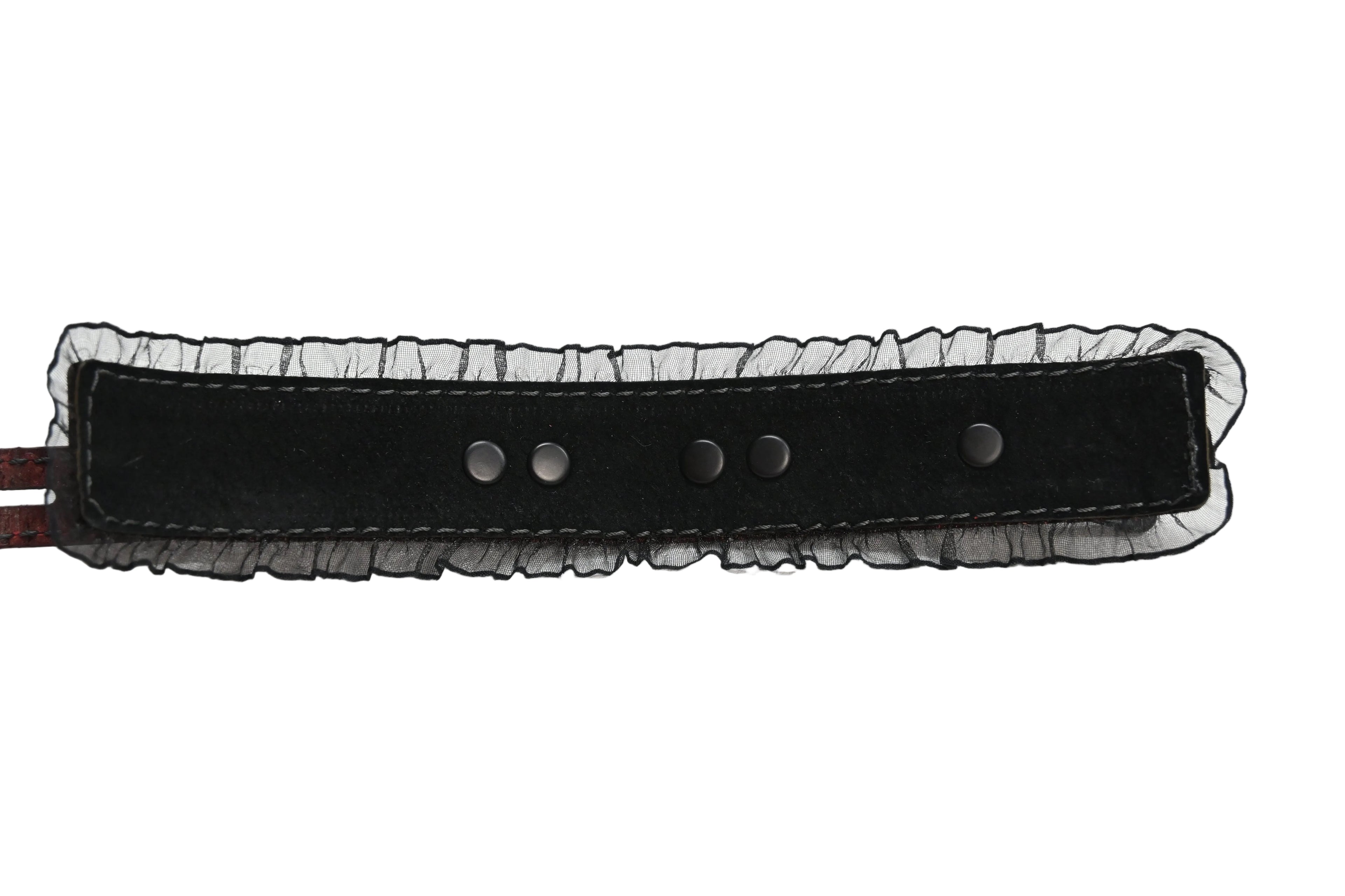 Interior photo of one of the cuffs showing a black suede lining and black ruffles along the edges, and black rivets. Photographed on a white background.