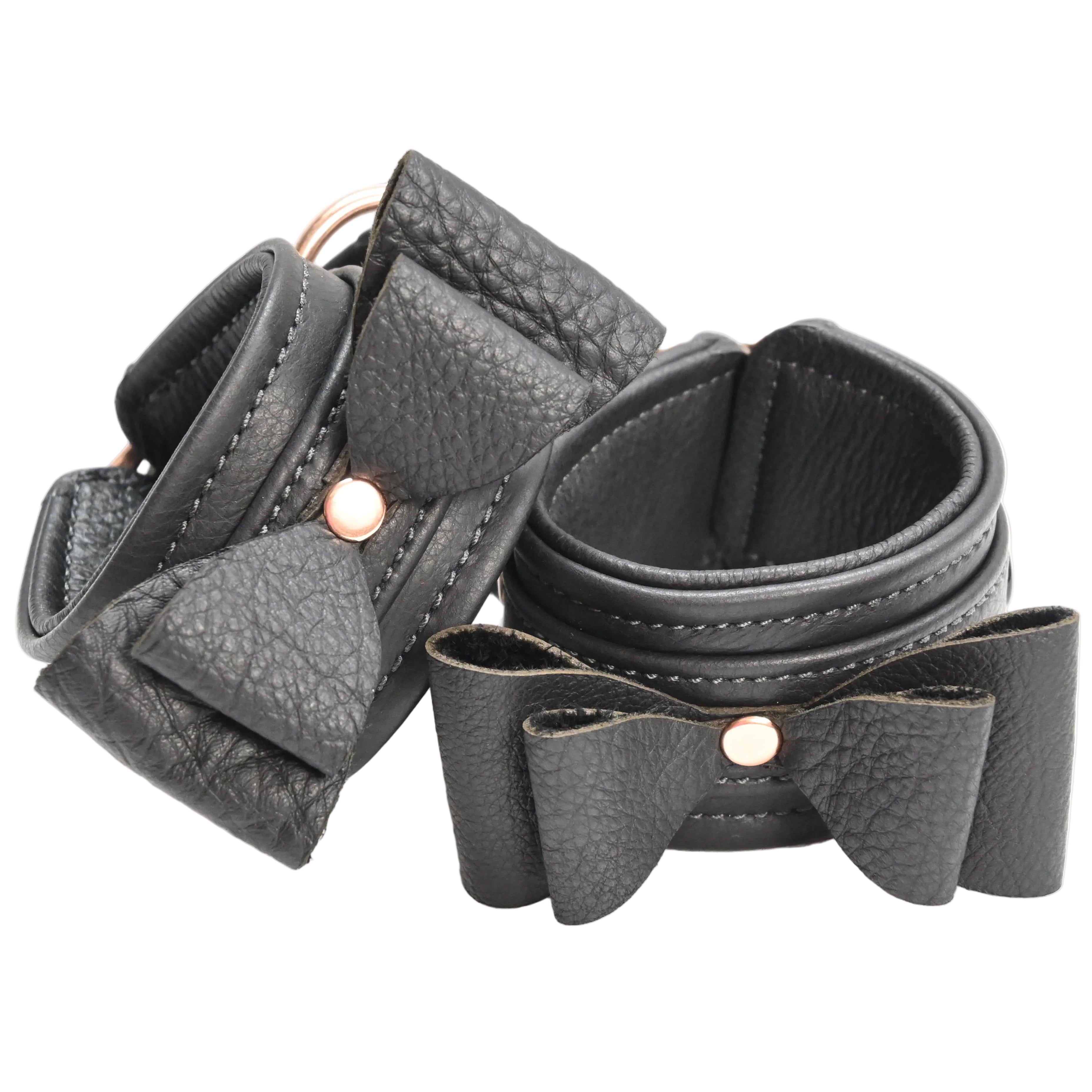 Two black leather wrist cuffs with bow details and rose gold metal hardware, displayed on a clean white background.