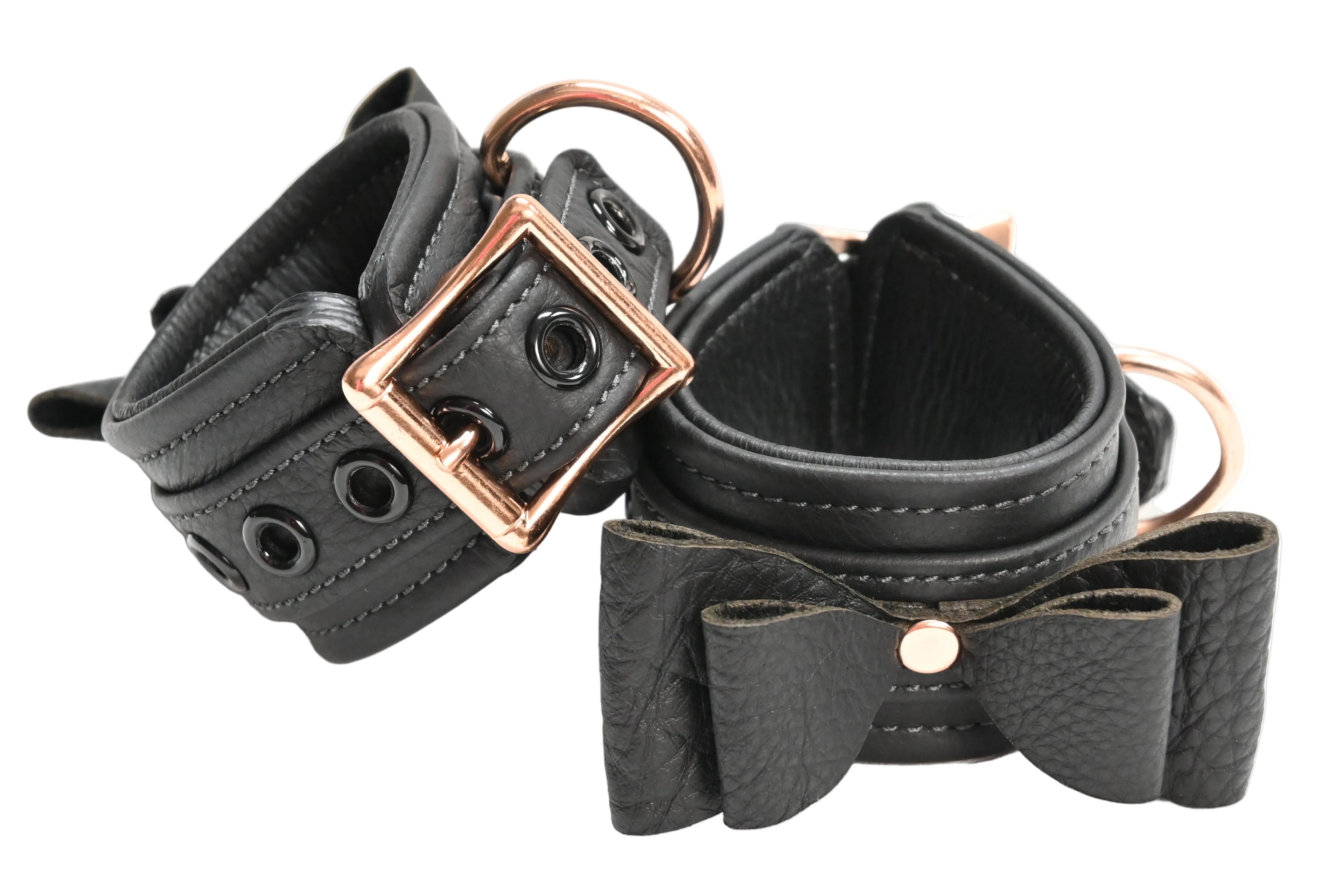 Two black leather wrist cuffs with bow details and rose gold metal hardware, displayed on a clean white background.