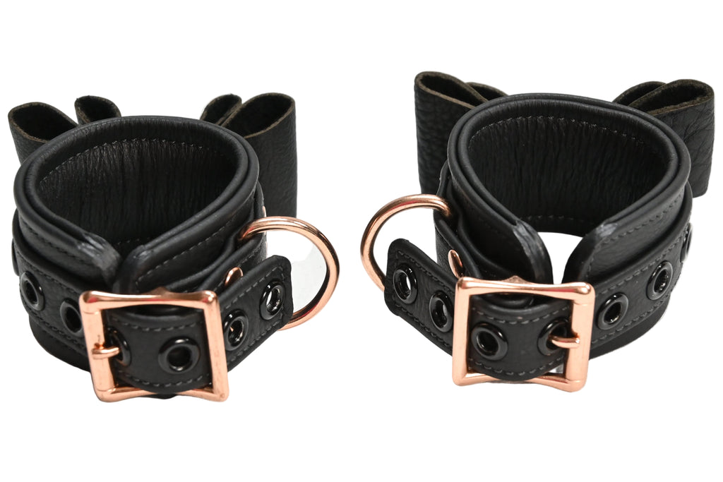Two black leather wrist cuffs with bow details and rose gold metal hardware, displayed on a clean white background.