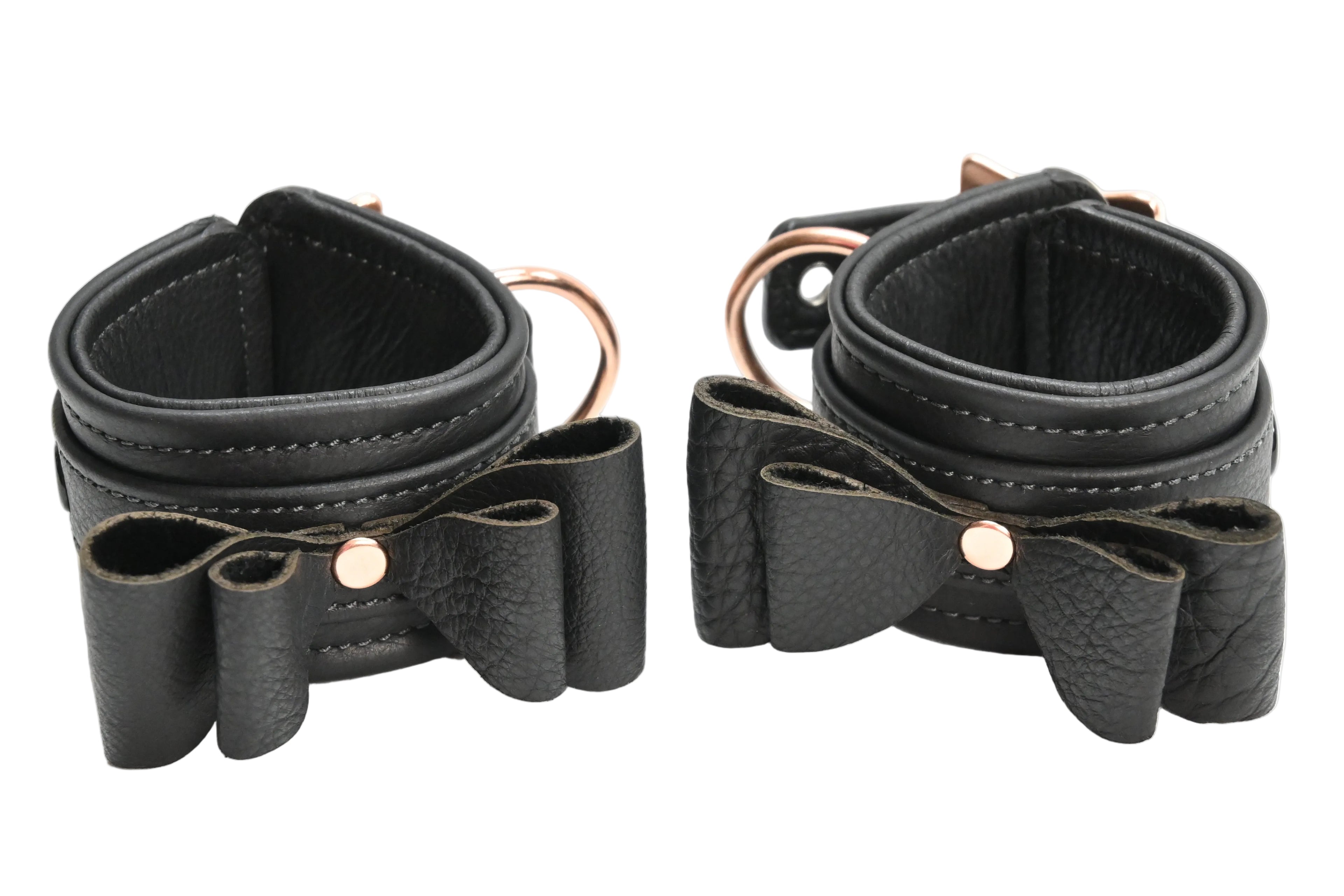 Two black leather wrist cuffs with bow details and rose gold metal hardware, displayed on a clean white background.