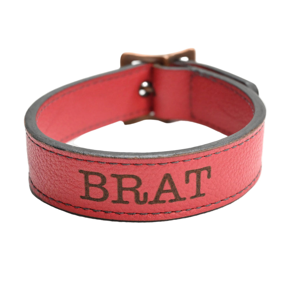 A red leather collar with the name 'BRAT' embossed on the front, shown on a plain white background.