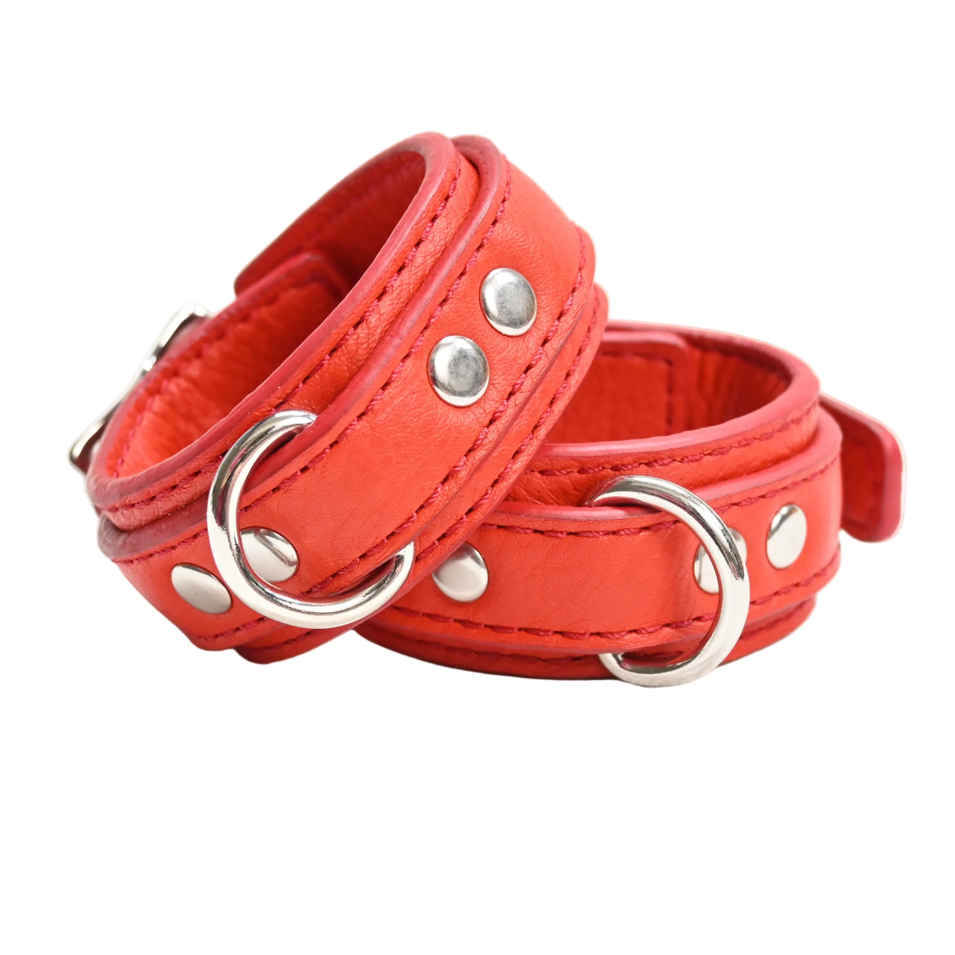 A bright red set of leather cuffs with silver-tone metal D rings and rivets, set on a white background.