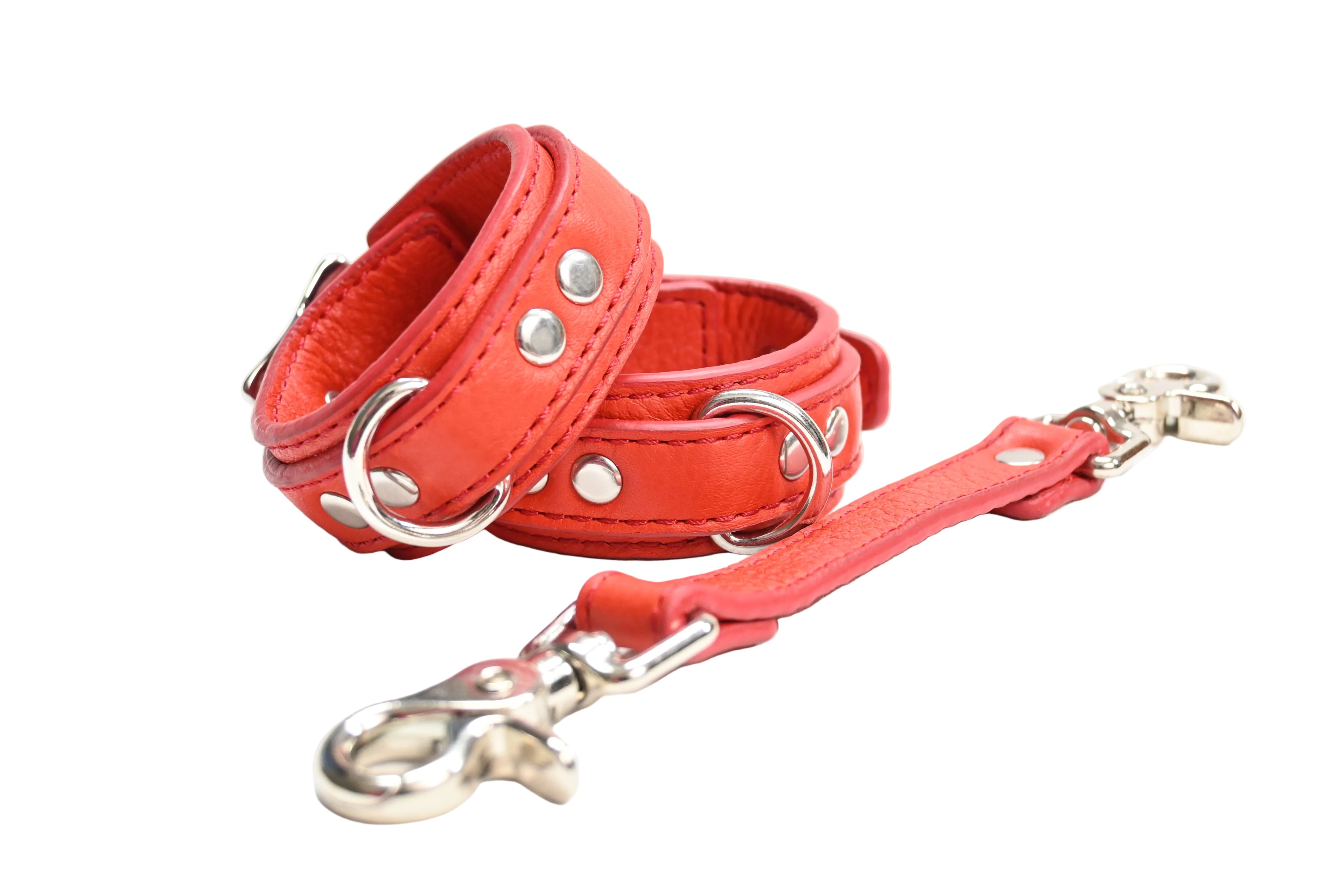 A bright red set of leather cuffs with matching link. Cuffs have silver-tone metal D rings and rivets, set on a white background.