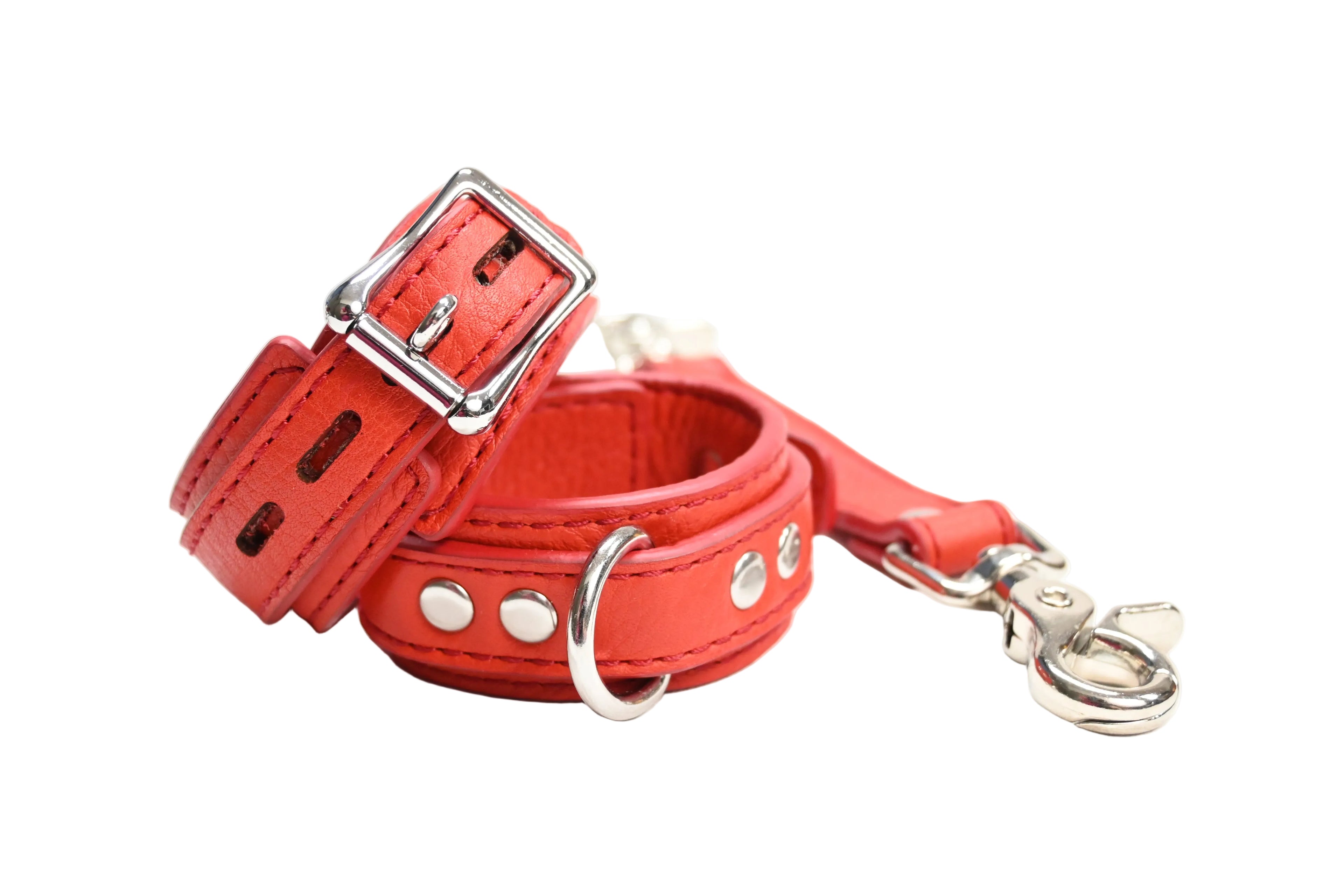A bright red set of leather cuffs with matching link. Cuffs have silver-tone metal D rings, buckles, and rivets, set on a white background.