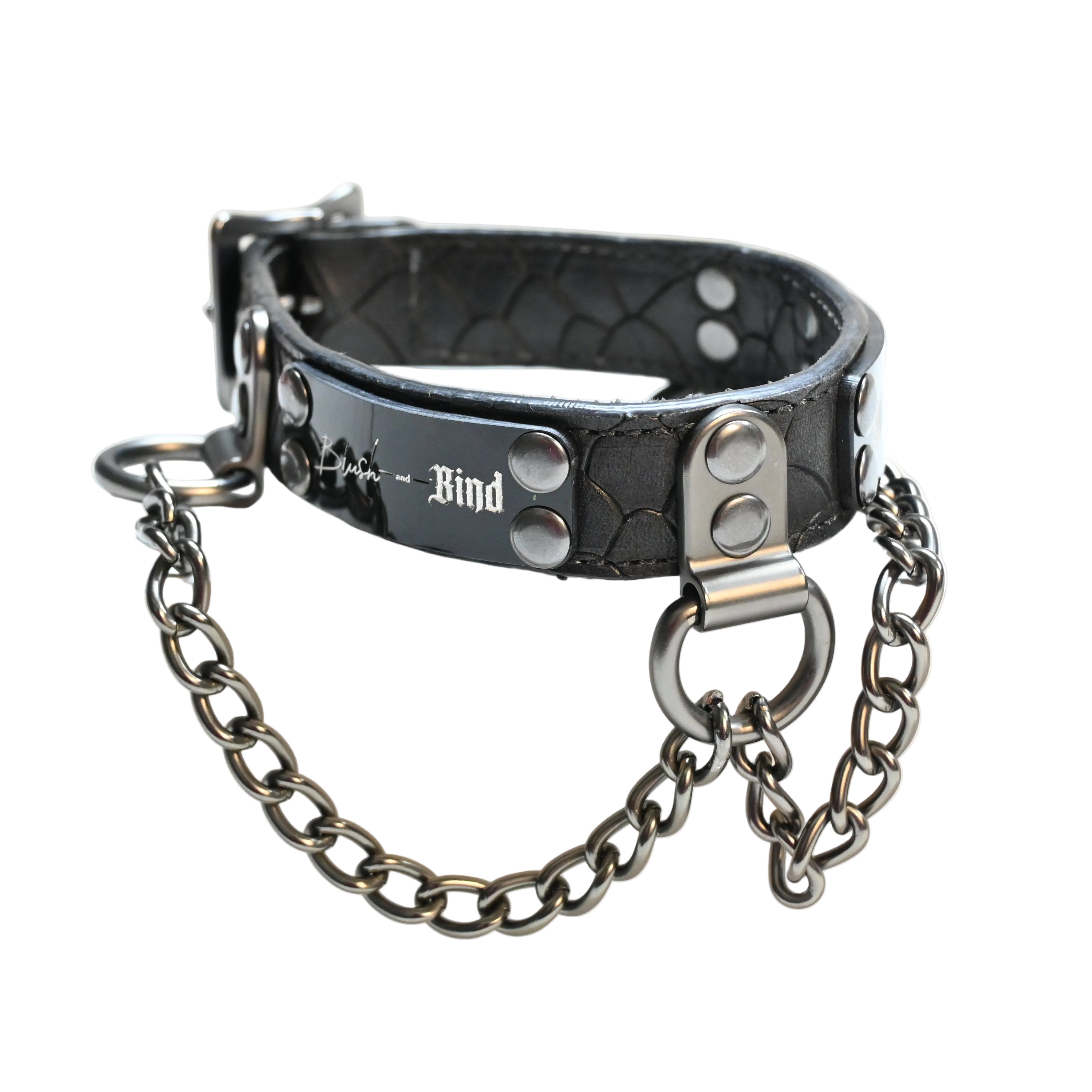 A black textured leather collar with silver hardware, featuring a chain and a plate engraved with 'Blush and Bind'  displayed on a white background.