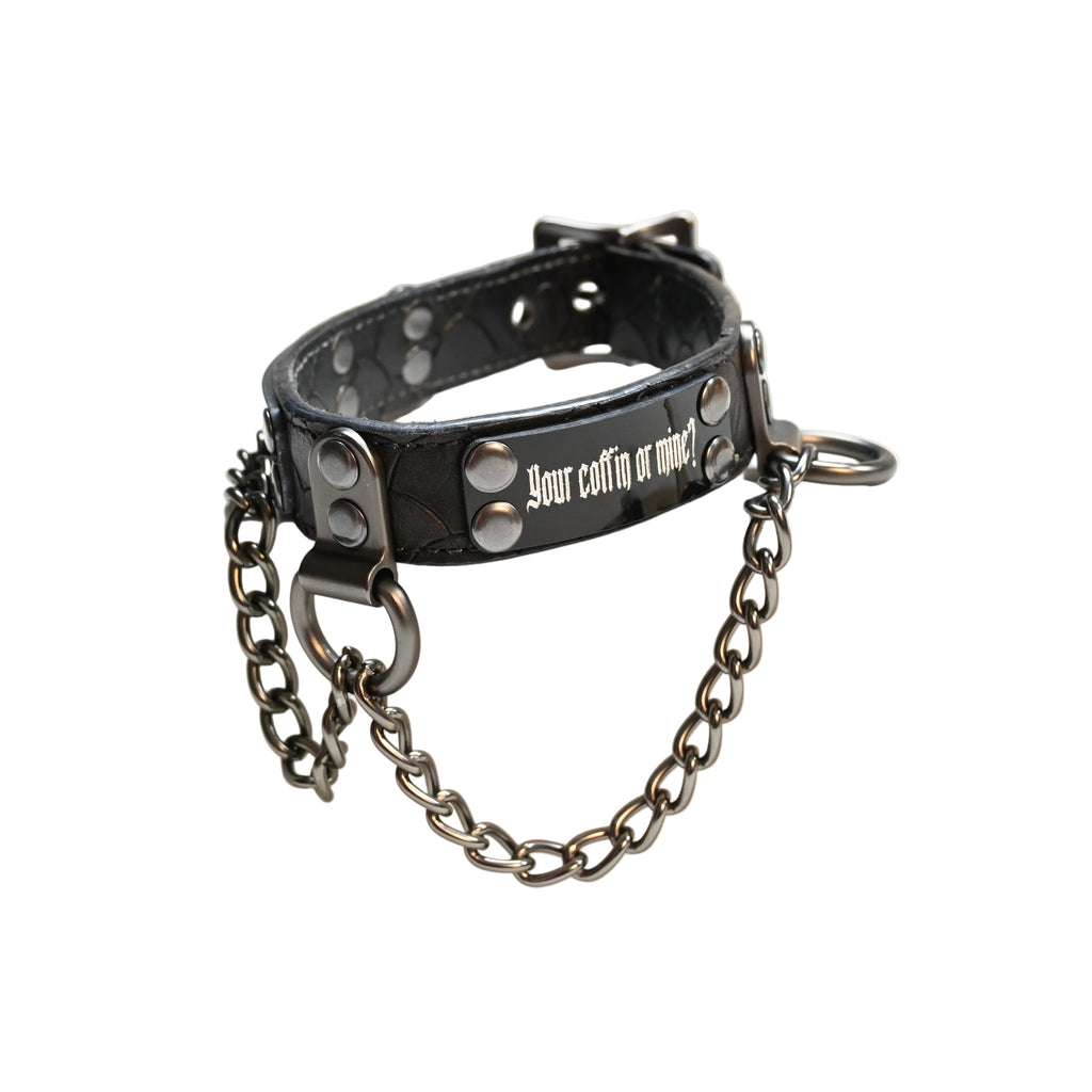 A black leather collar with silver studs and a dark metal chain, displayed on a white background. The collar features the text 'your coffin or mine?'