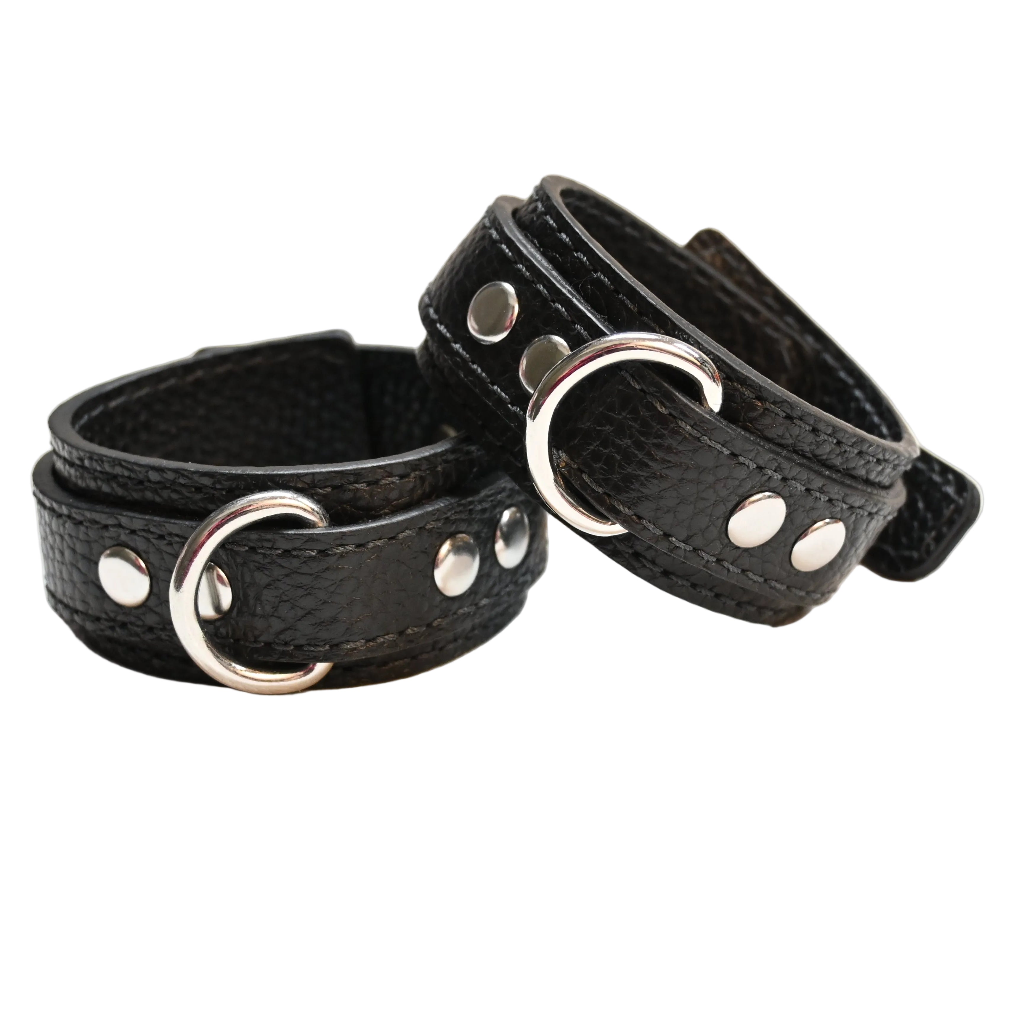 Two black leather cuffs with silver metal D rings and rivets, displayed on a clean white surface.