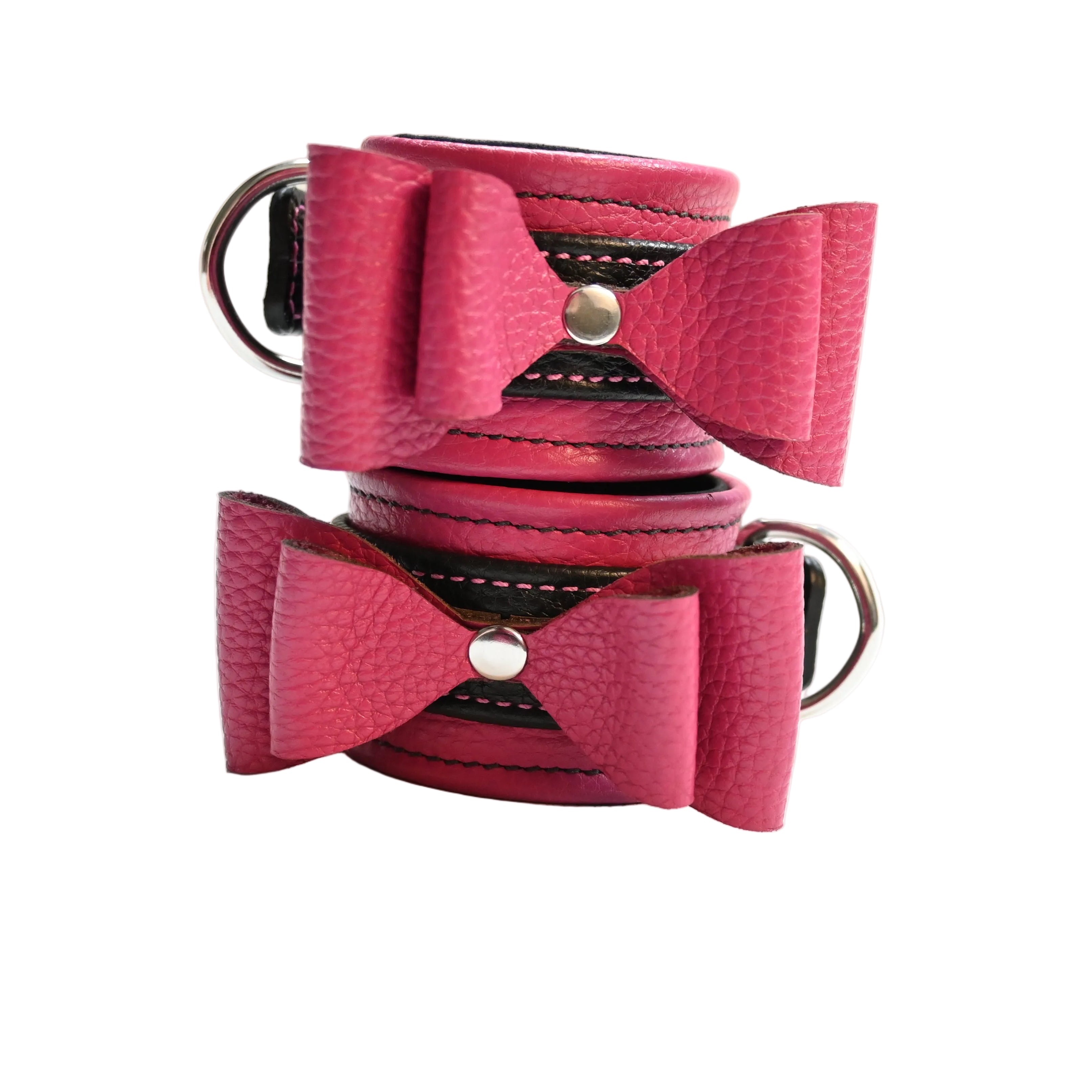 Two pink and black leather bow cuffs with black lining and silver hardware, displayed stacked on a white background.