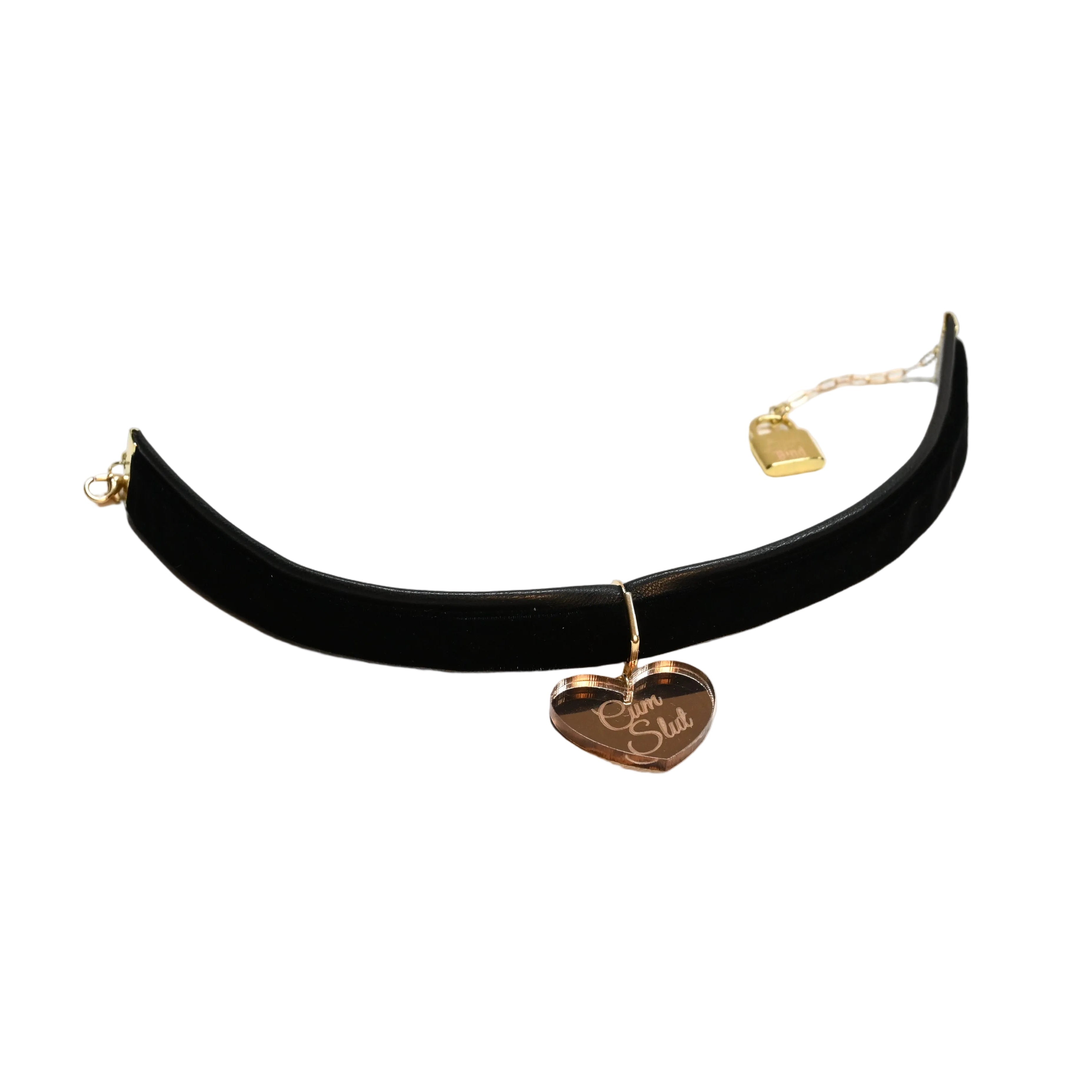 A black velvet choker collar with gold hardware, featuring a dangling heart-shaped tag engraved with 'C*m Sl*t' and a small gold padlock charm, displayed on a white background.