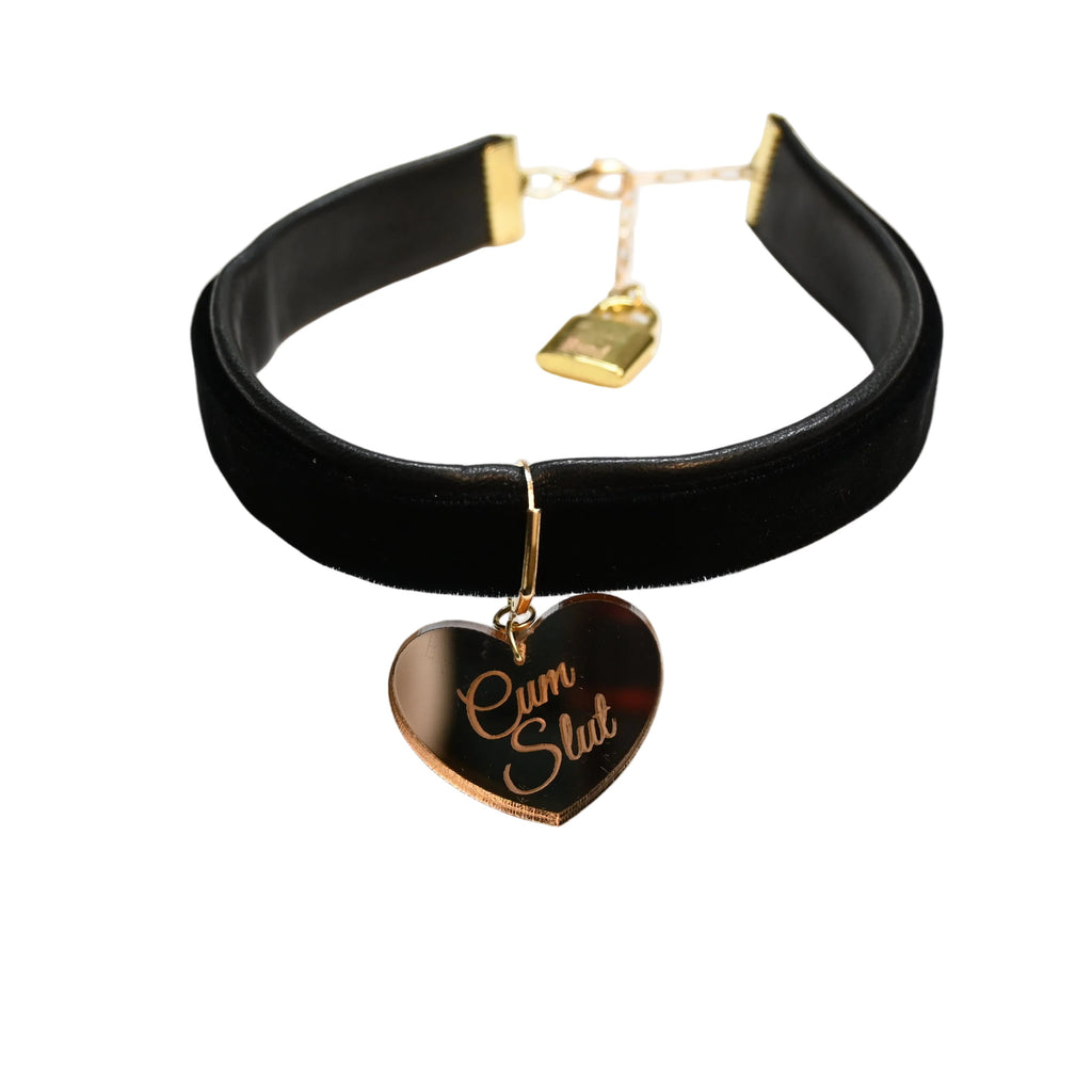 A black velvet choker collar with gold hardware, featuring a dangling heart-shaped tag engraved with 'C*m Sl*t' and a small gold padlock charm, displayed on a white background.