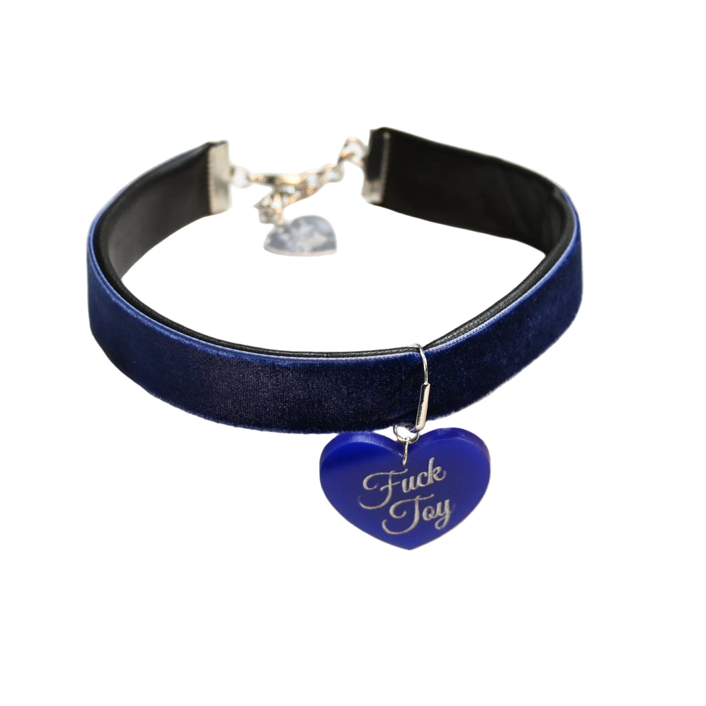 A dark blue velvet choker collar with a silver-tone metal clasp and a blue heart-shaped charm engraved with the words 'Fuck Toy' in white script, displayed on a white background.