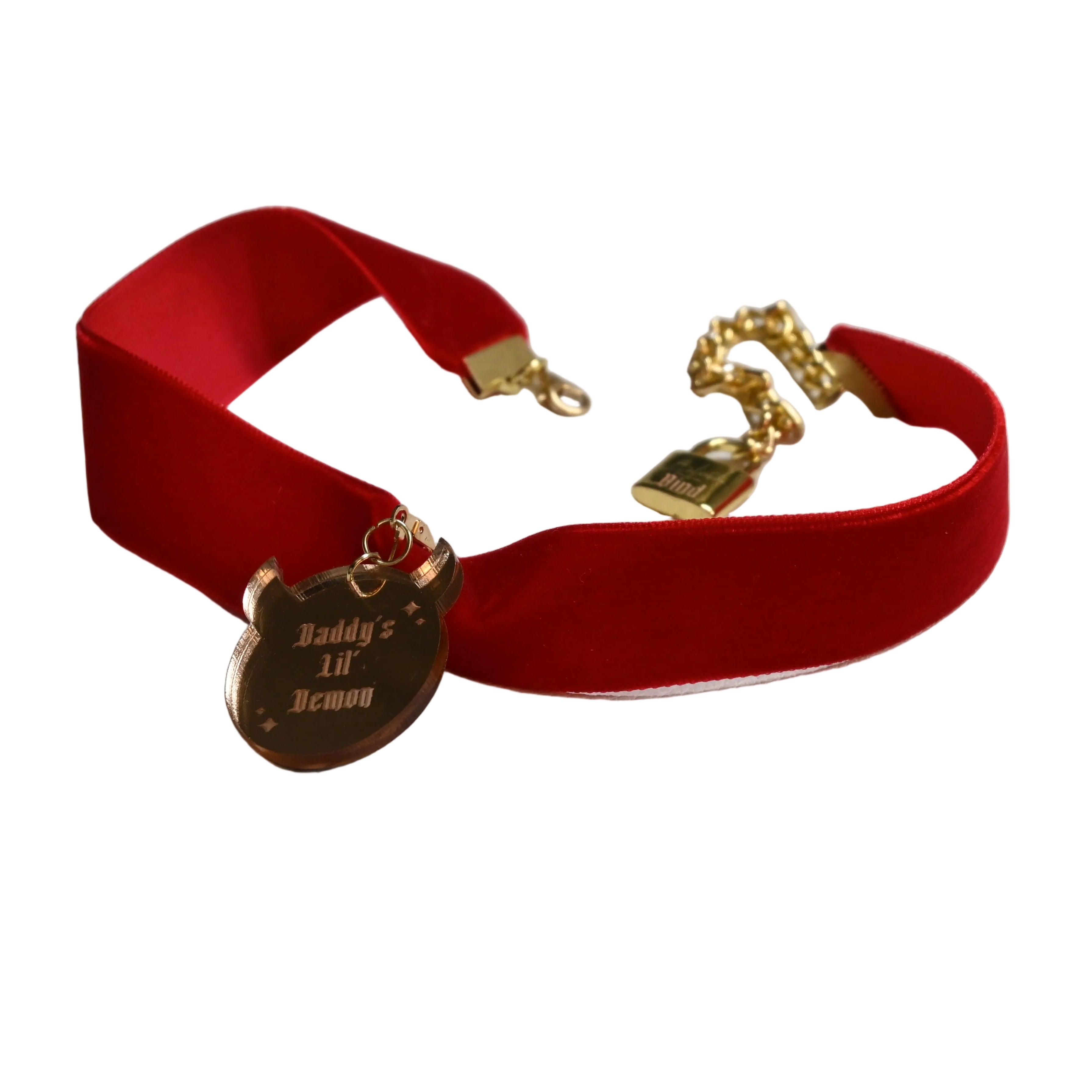 A red velvet choker collar with gold-tone hardware, featuring a pendant engraved with 'Daddy's lil' demon' and a gold chain clasp.