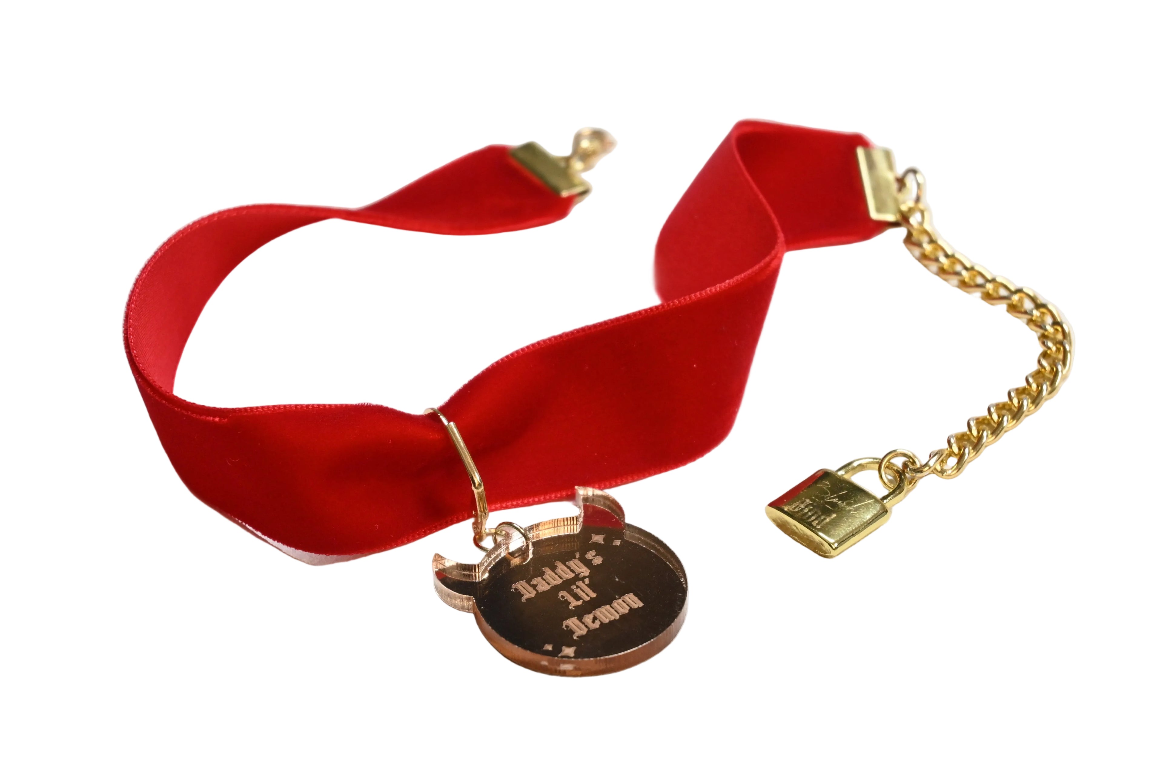 A red velvet choker collar with gold-tone hardware, featuring a pendant engraved with 'Daddy's lil' demon' and a gold chain clasp.