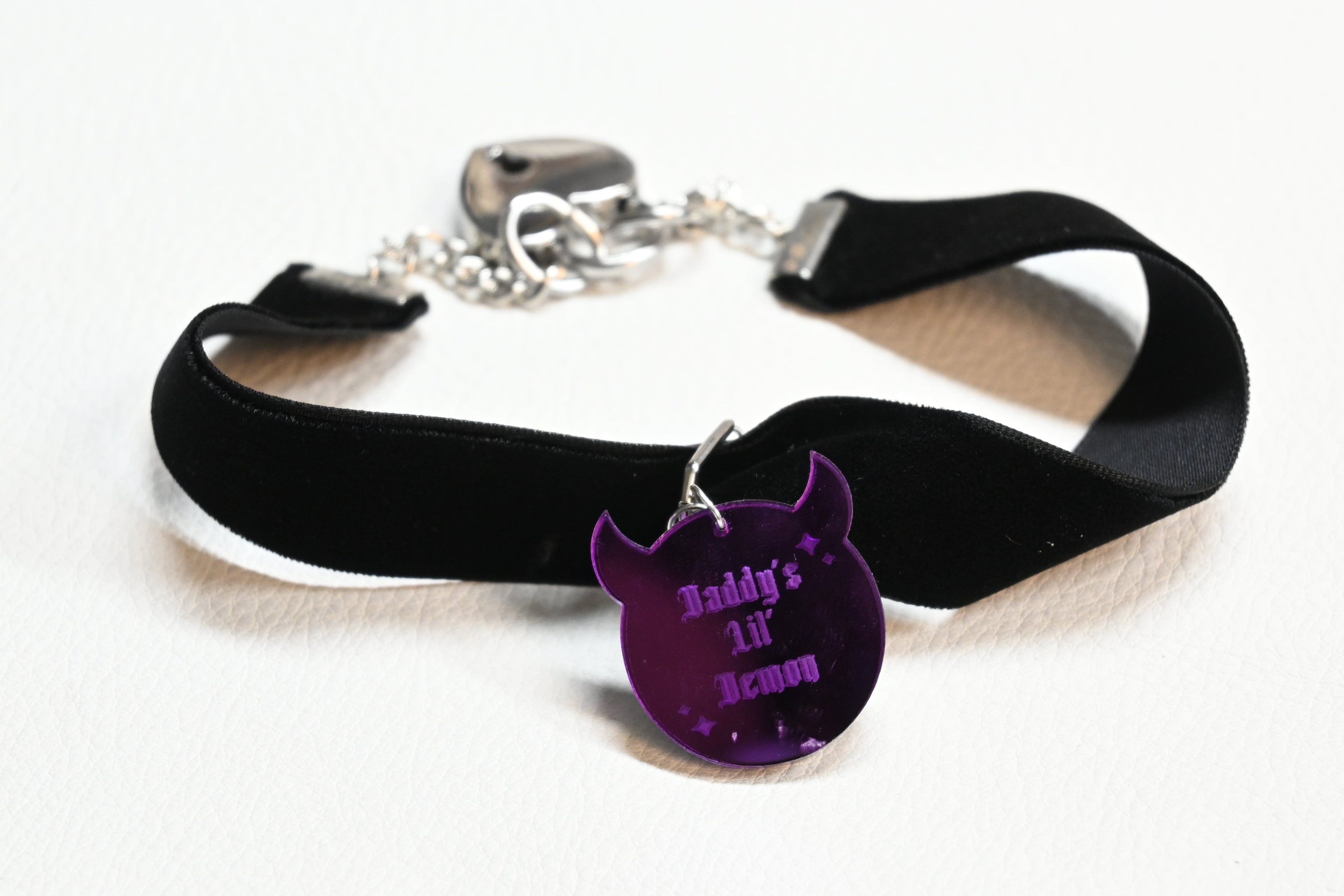 A black velvet collar with a silver clasp and a purple demon-shaped charm engraved with 'Daddy's LIL' Demon', displayed on a white background.